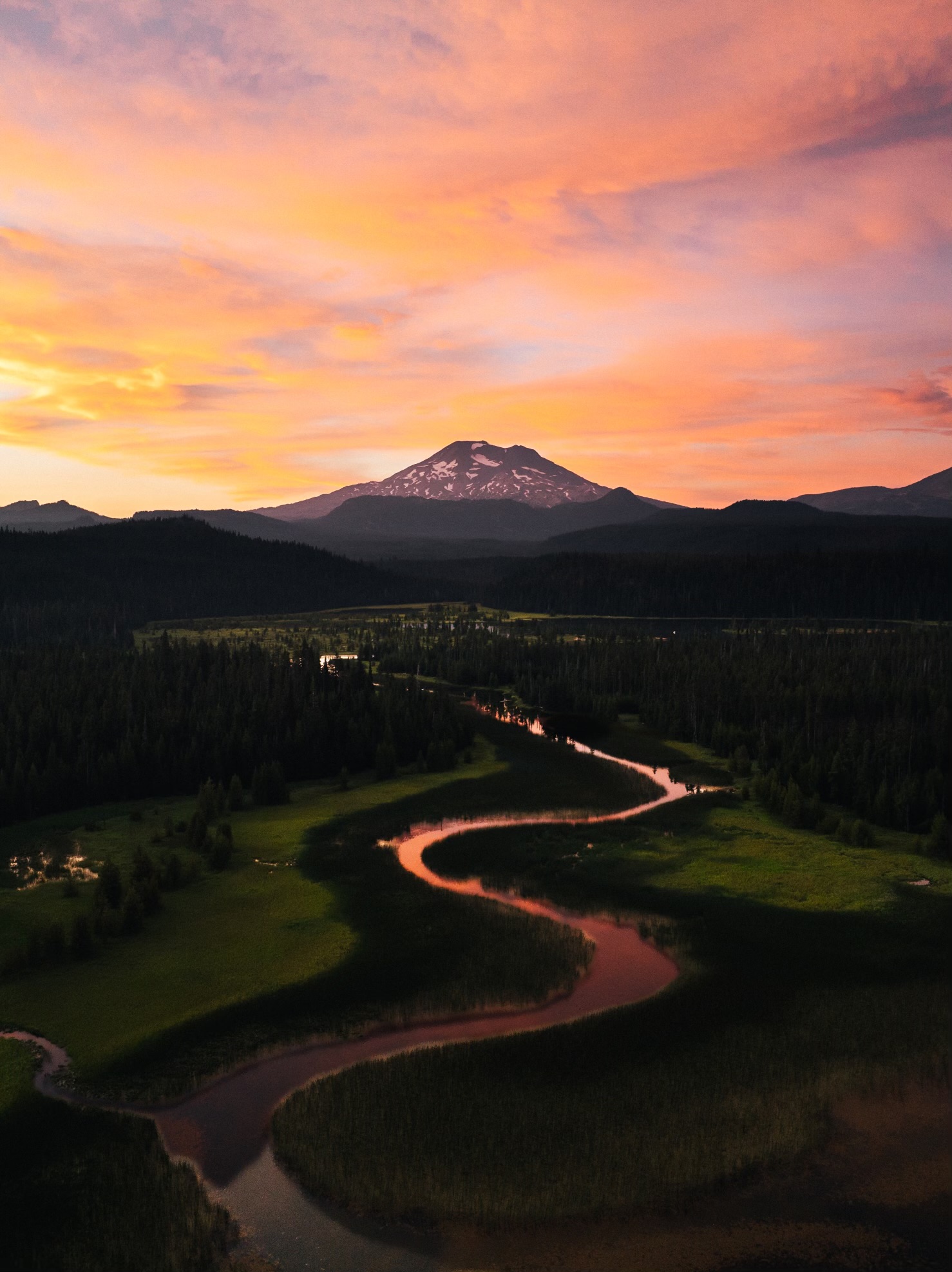 A winding river reflecting a colorful sunset below a mountain